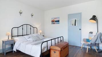 Una camera da letto con un letto, comodino, lampada, cassettiera, sedia e una porta.