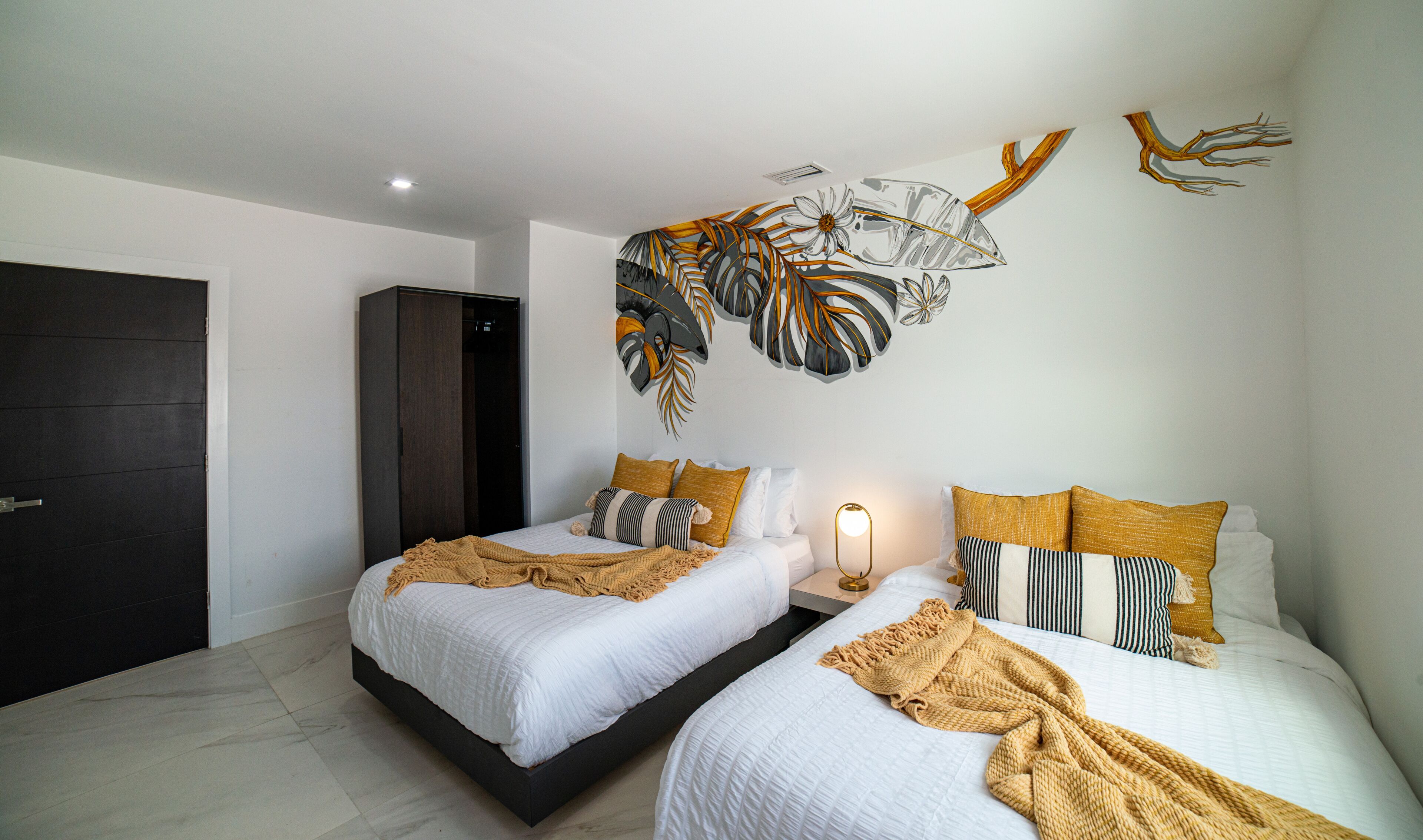Quarto moderno com duas camas, um guarda-roupa escuro e um mural na parede.