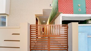 A gated entrance with a wooden gate, a tiled floor, and a building with a beige wall and a red brick section.