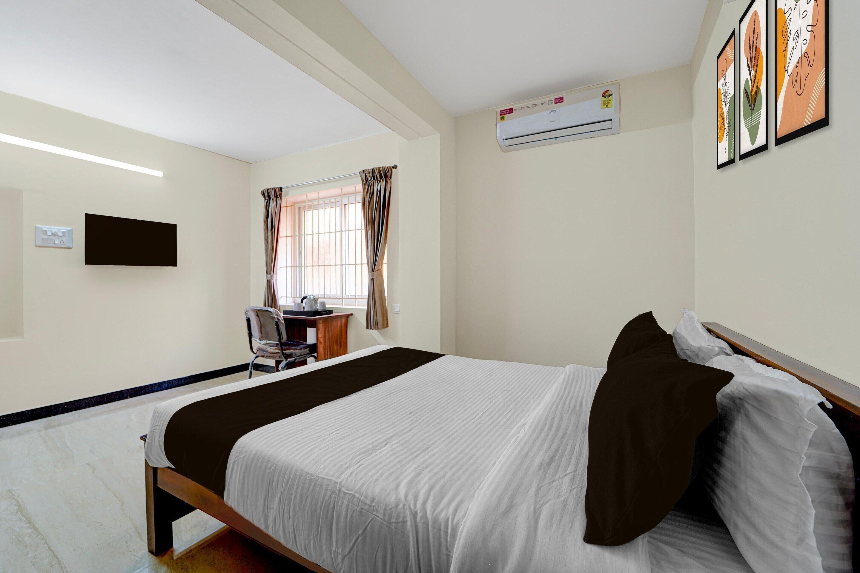 Ein Hotelzimmer mit Bett, Schreibtisch, Sessel, Klimaanlage und Fernseher.