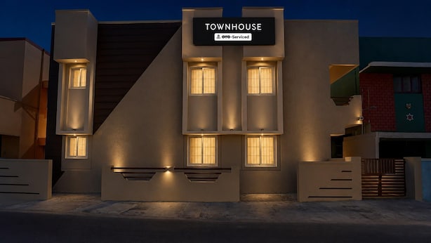 A modern townhouse with a sign reading 'TOWNHOUSE' and 'OYO-Serviced.' It features multiple windows and a flat roof.