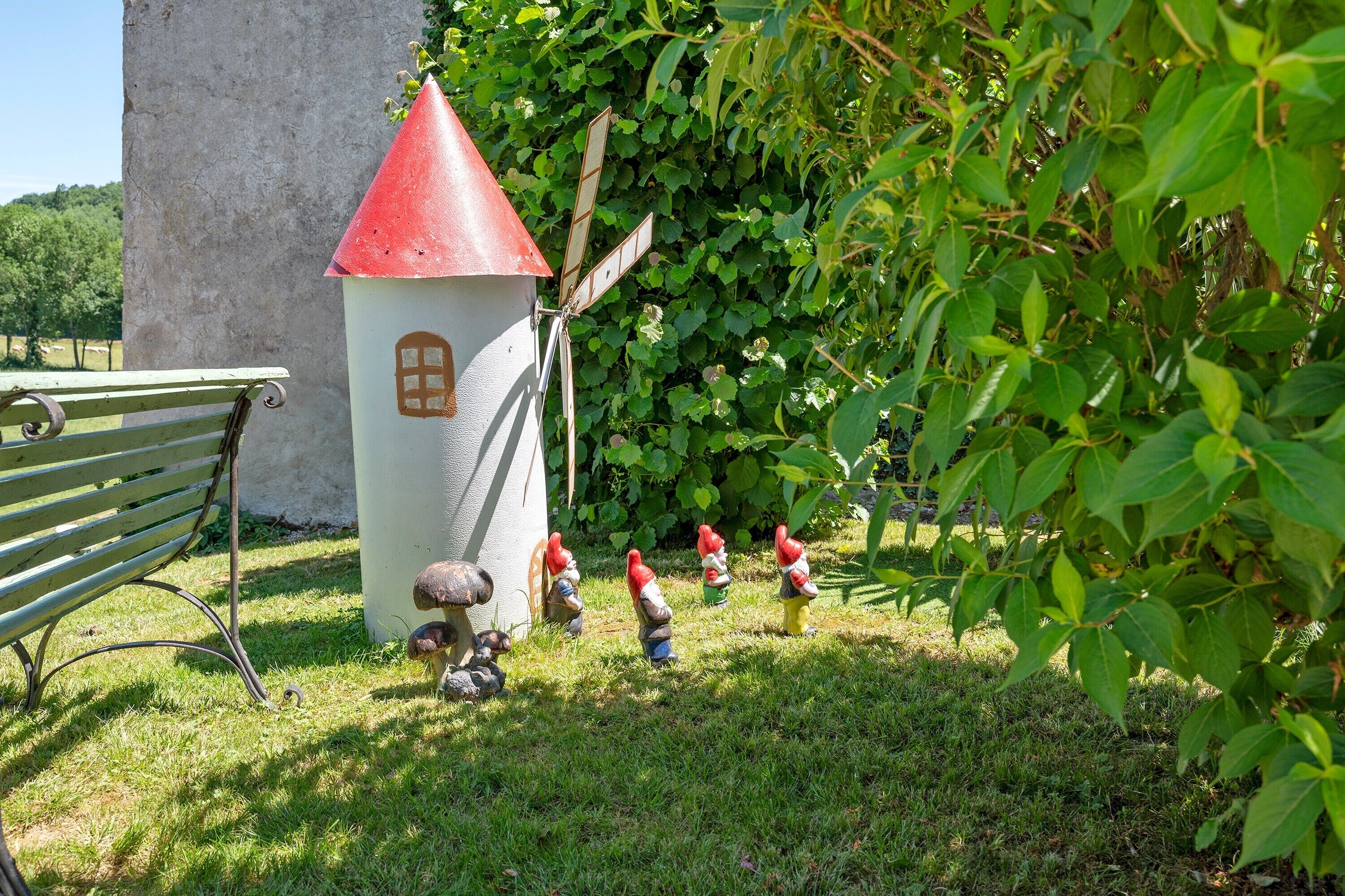 A garden with a white structure with a red roof, a bench, and gnome statues.