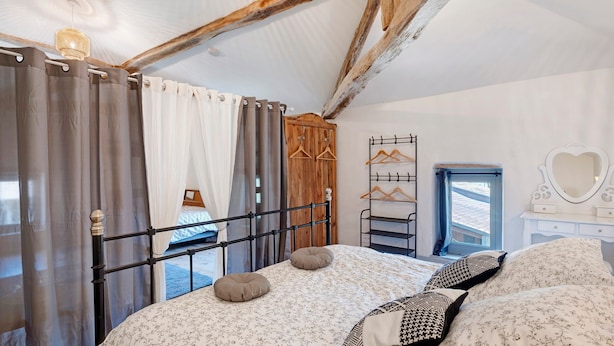 A bedroom with a bed, curtains, a wooden wardrobe, a mirror, and a window.