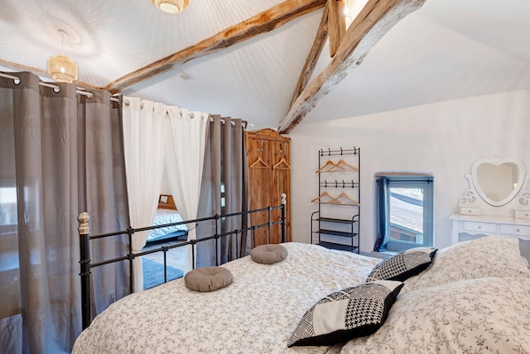 A bedroom with a bed, curtains, a wooden wardrobe, a mirror, and a window.