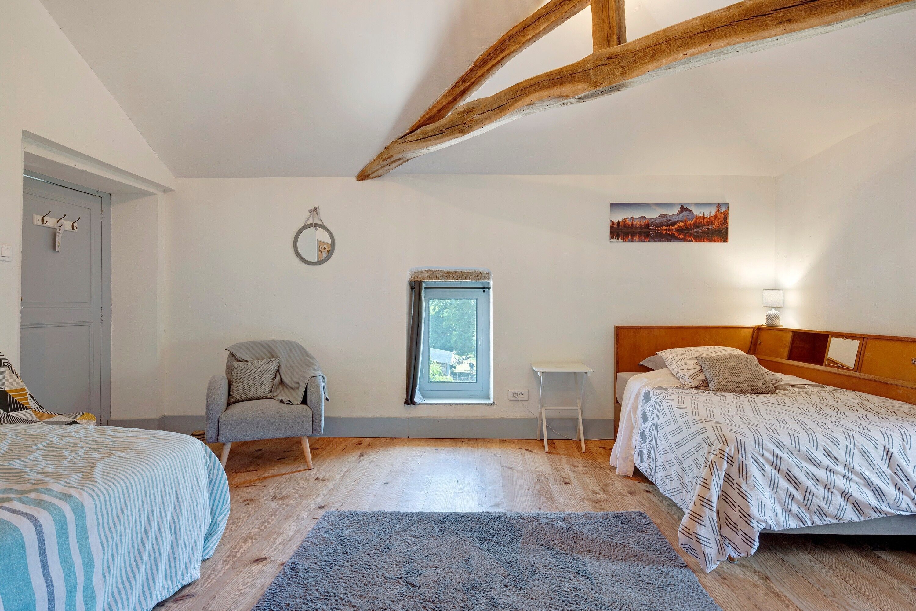 Une chambre avec deux lits, une chaise, une petite table, une fenêtre et un tableau au mur.