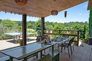 An outdoor patio with a wooden table set for dining, surrounded by chairs, and a view of a forested landscape.