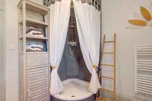 A bathroom with a shower, a toilet, a sink, a wooden ladder, and a storage unit with towels.