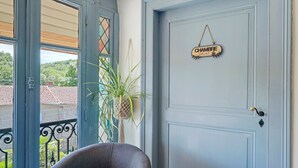 A room with a blue door, a sign reading 'CHAMBRE SALAT,' a potted plant, and a view of a balcony with a railing.