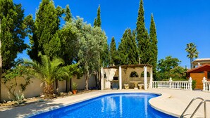A swimming pool with a stone structure, surrounded by trees and a white fence. - Private Pool Villa La Siesta (Torrevieja)
