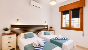 A hotel room with two beds, a wooden headboard, an air conditioning unit, bedside lamps, a window with a view, and a small table with a plant. - Private Pool Villa La Siesta (Torrevieja)