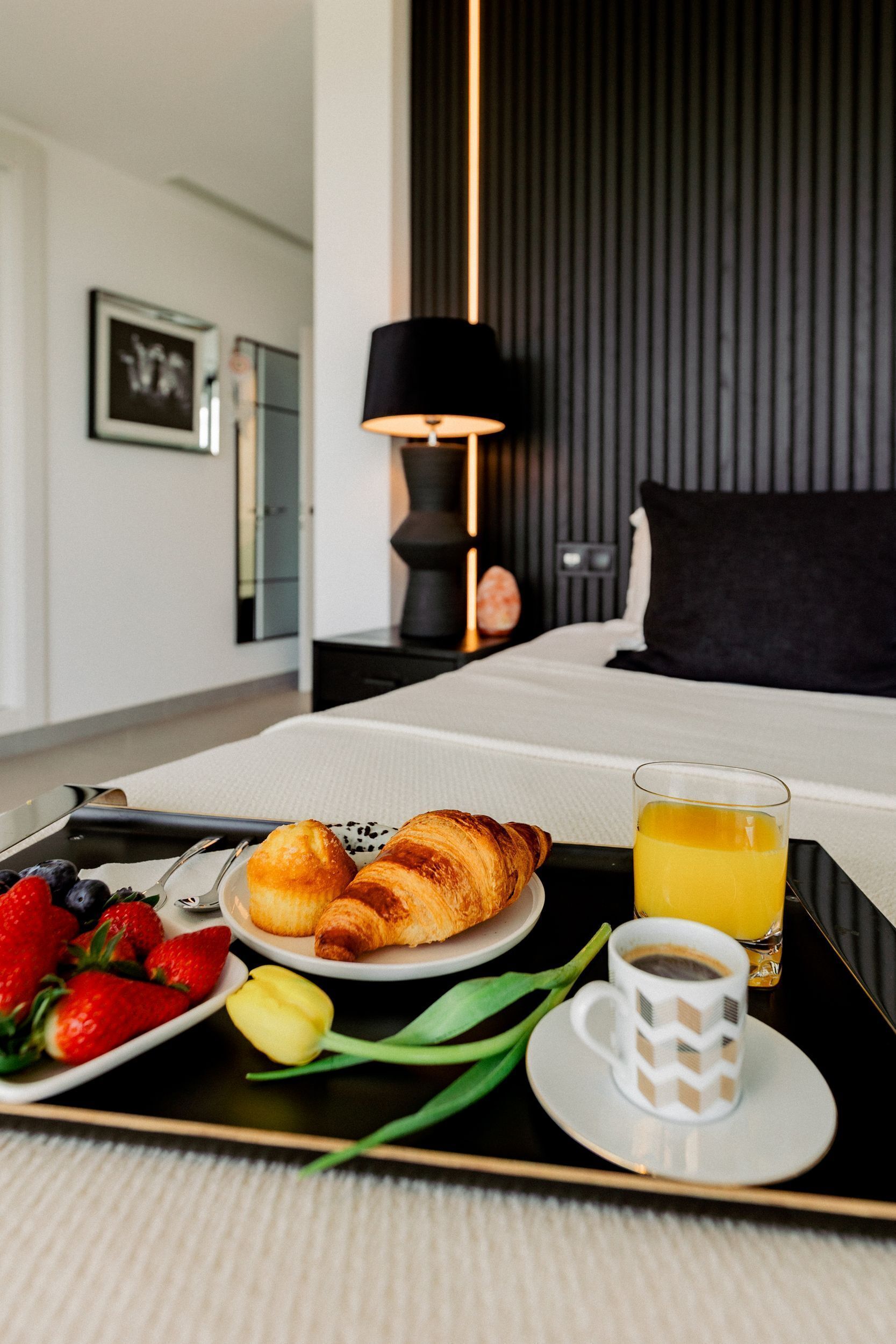 Un plateau de petit-déjeuner soigneusement préparé, avec des croissants, des fraises, une tulipe et un verre de jus d’orange, est posé sur une table dans une chambre d’hôtel.