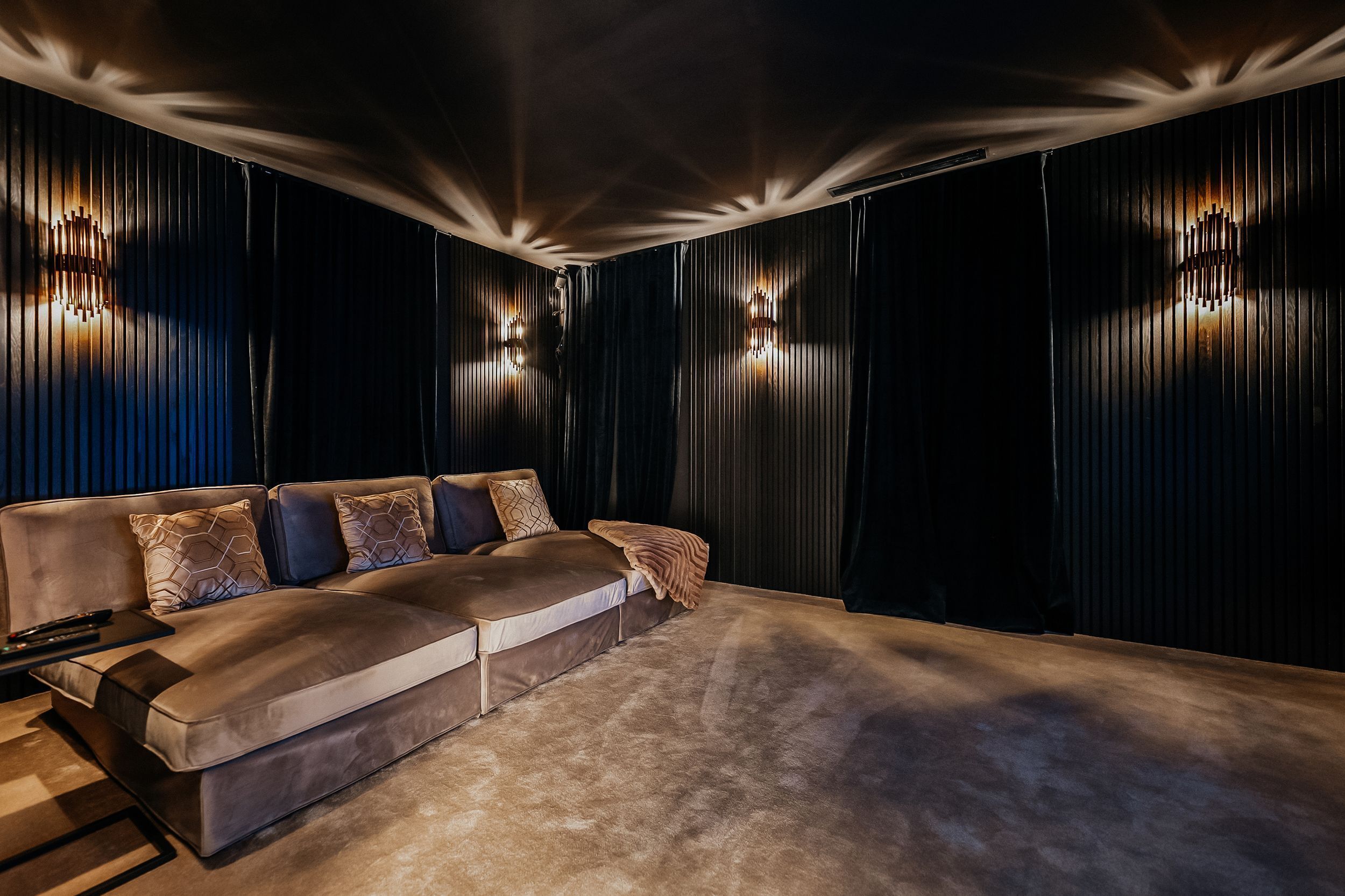 Een moderne woonkamer met een hoekbank, wandlampen en een gestructureerd plafond.