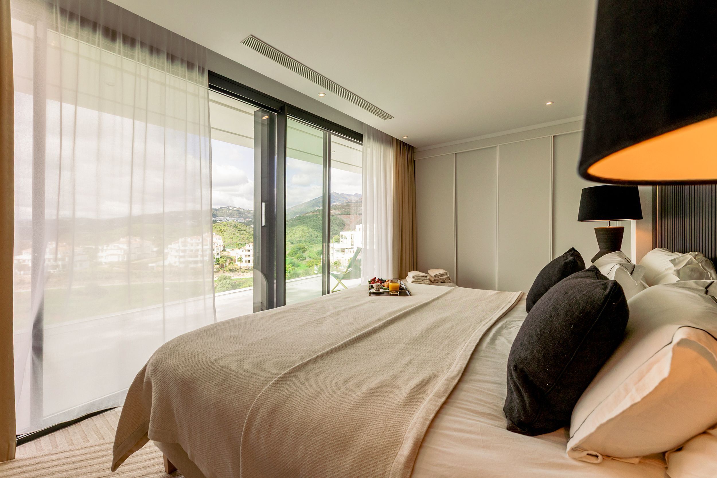 A hotel room with a large bed, a nightstand, a lamp, and a view of the outdoors.