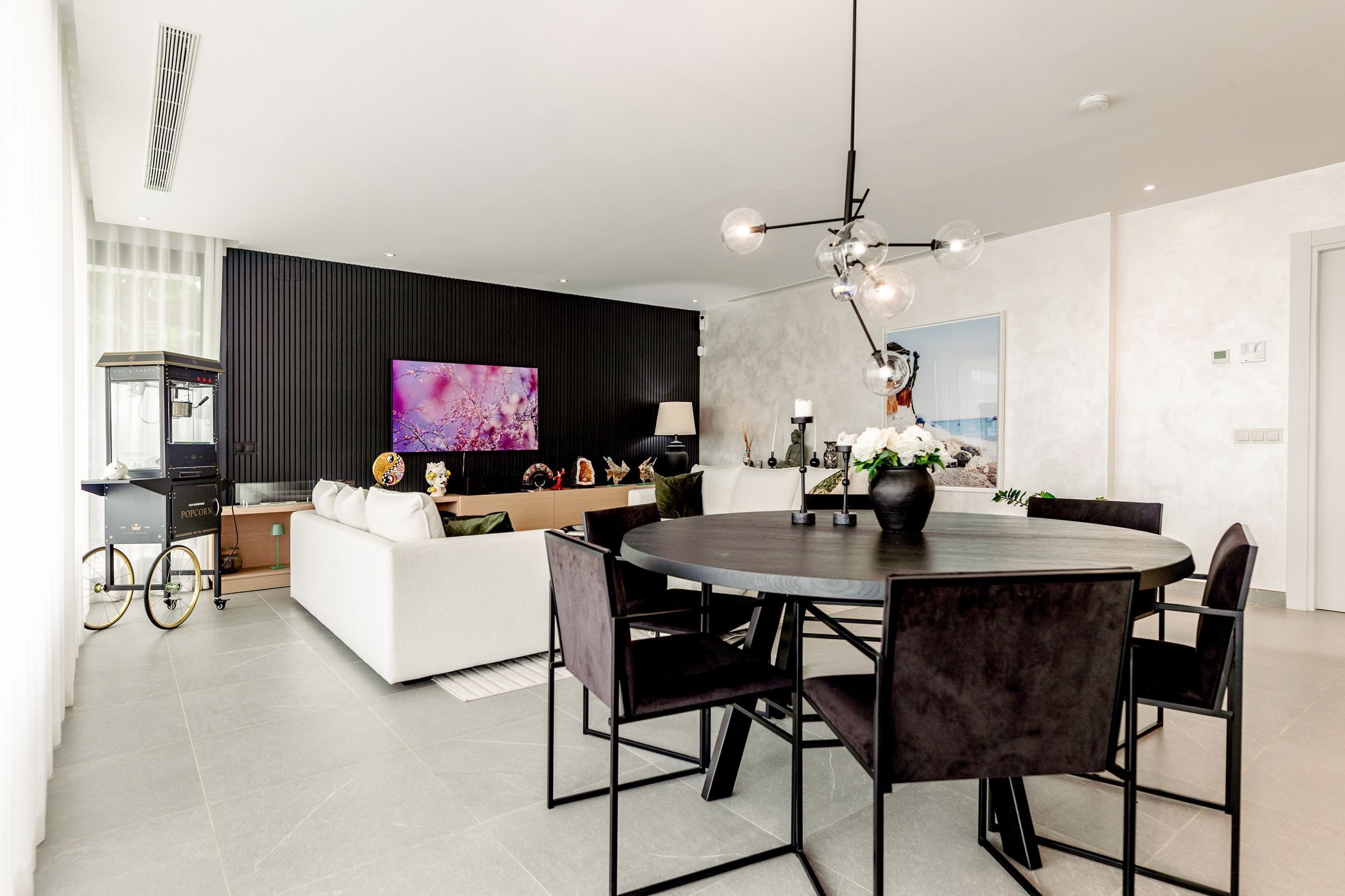 A modern living room with a dining area, a large flat-screen TV, and a black wall with a decorative panel.