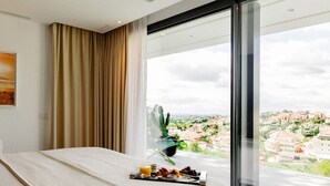 A modern hotel room with a large bed, a view of the city, and a dining area with a tray of food. - Modern Luxury Villa with Panoramic  View (Marbella)