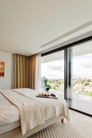 A modern hotel room with a large bed, a view of the city, and a dining area with a tray of food. - Modern Luxury Villa with Panoramic  View (Marbella)