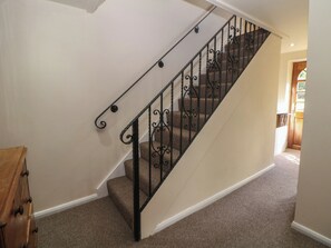 Eine Teppich-Treppe mit schwarzem schmiedeeisernen Geländer, ein Holzmöbelstück auf der linken Seite und eine Tür am Fuß der Treppe.