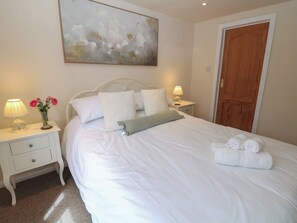 Una cama bien hecha con almohadas y una colcha, una mesita de noche con una lámpara y un florero, y un cuadro en la pared.