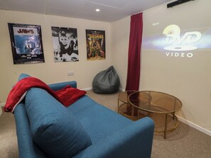 Ein Zimmer mit einem blauen Sofa, einer roten Decke, einem grauen Sitzsack, einem Glastisch und Filmplakaten an der Wand.