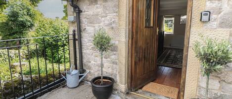 A stone building with a wooden door, potted plants, and a metal railing.
