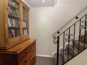 Una escalera con barandilla de hierro forjado, una estantería de madera con libros y un aparador de madera.