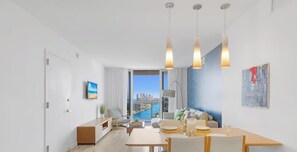 A modern living room with a dining area, large windows with a city view, and a minimalist decor. - Top-Floor Waterway 2BR · Beachwalk Resort FL (Hallandale Beach)