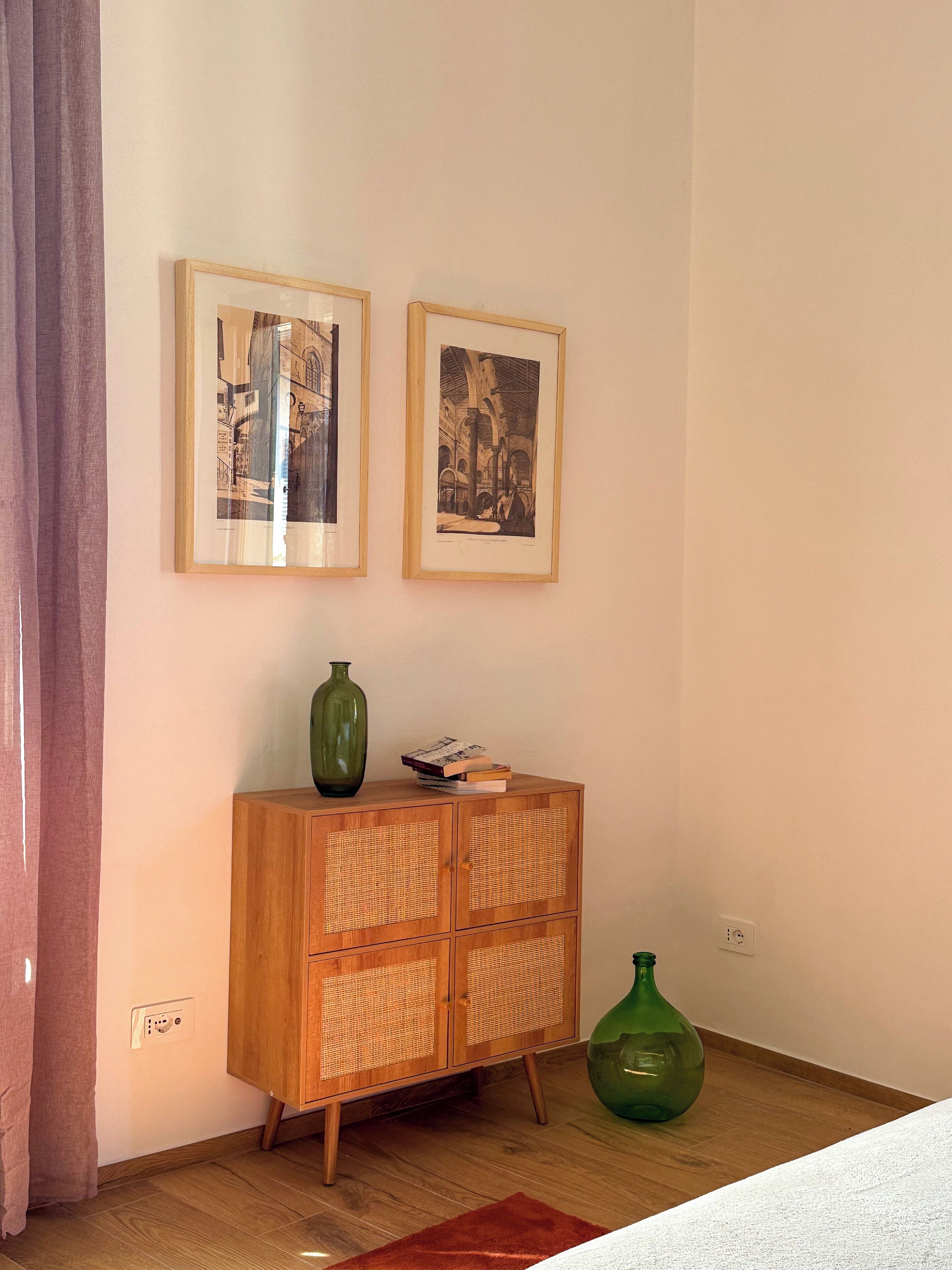 Una habitación con un aparador de madera, dos cuadros enmarcados y dos jarrones verdes.