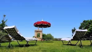 Twee lounge stoelen met een rode parasol, een stenen toren en een heldere blauwe lucht.
