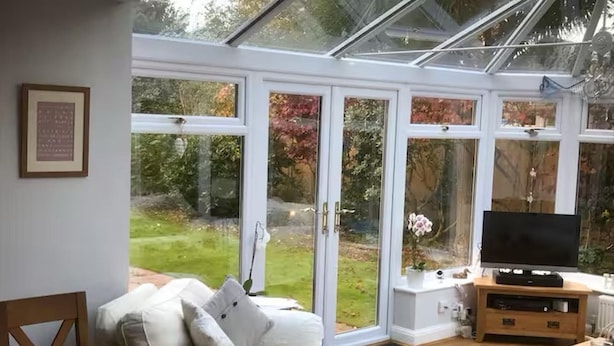 A conservatory with a sofa, TV, and dining table. - House Sleeps 9 With Indoor Pool (Chichester)