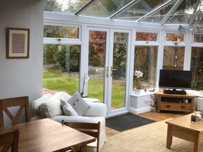 A conservatory with a sofa, TV, and dining table.