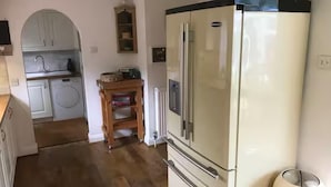 A kitchen with a large white refrigerator, a wooden cabinet, and a washing machine. - House Sleeps 9 With Indoor Pool (Chichester)