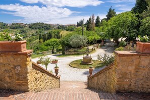 A stone staircase leading to a courtyard with potted plants and a view of a hilly landscape.