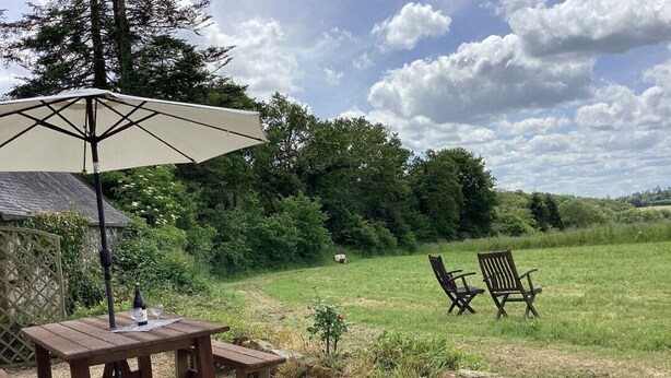 Een houten picknicktafel met een parasol, twee stoelen en een fles wijn.