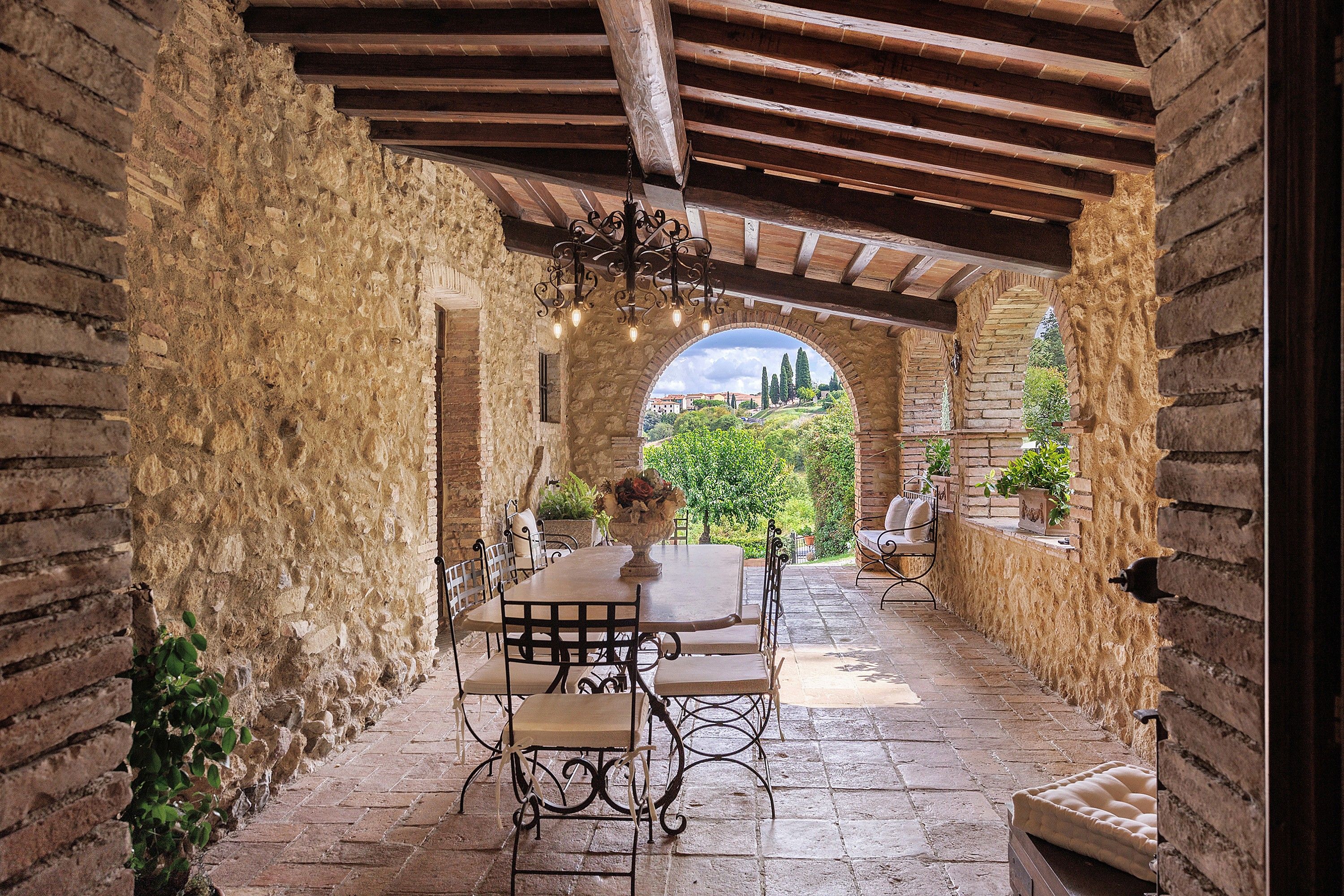 Patio esterno con tavolo e sedie, pareti in pietra e vista sul verde.