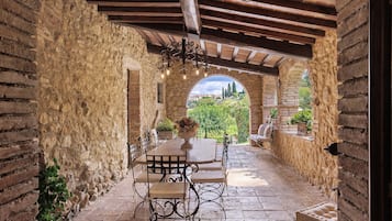 Patio esterno con tavolo e sedie, pareti in pietra e vista sul verde.