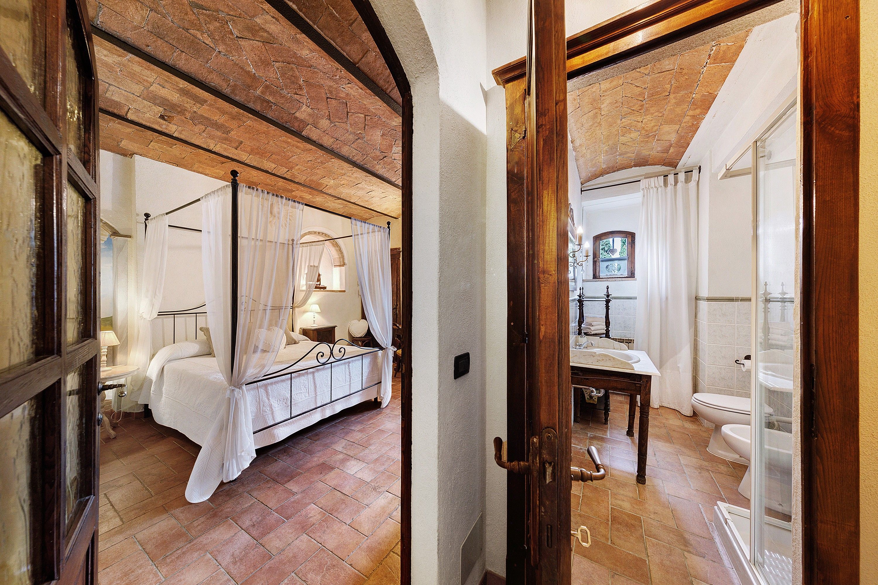 A bedroom with a four-poster bed, a nightstand, and a window with curtains.