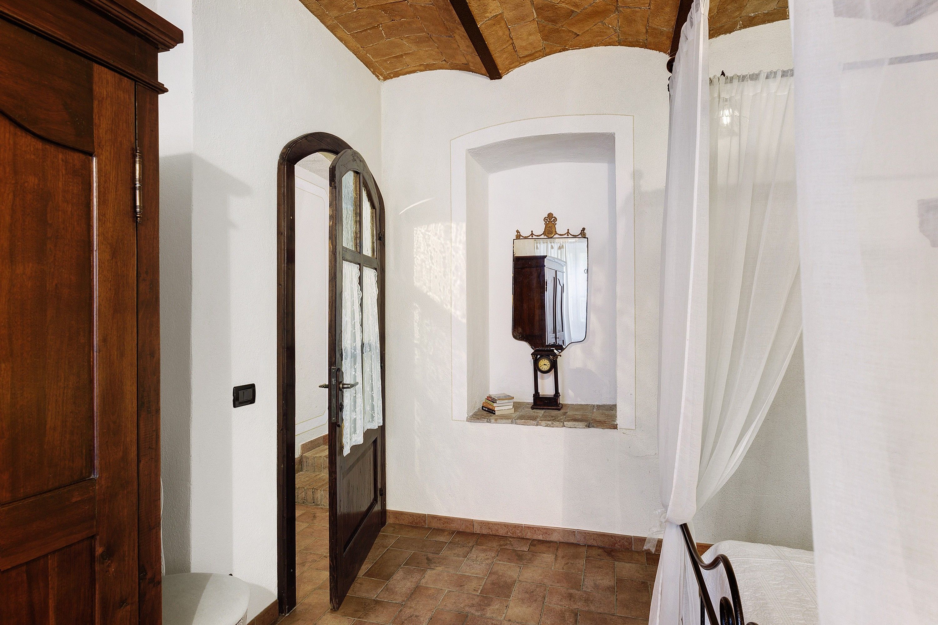 Un corridoio con una porta in legno, uno specchio con un orologio e una finestra con una tenda.