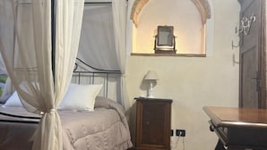 Una camera da letto con un letto, un comodino, un tavolo e una finestra ad arco.