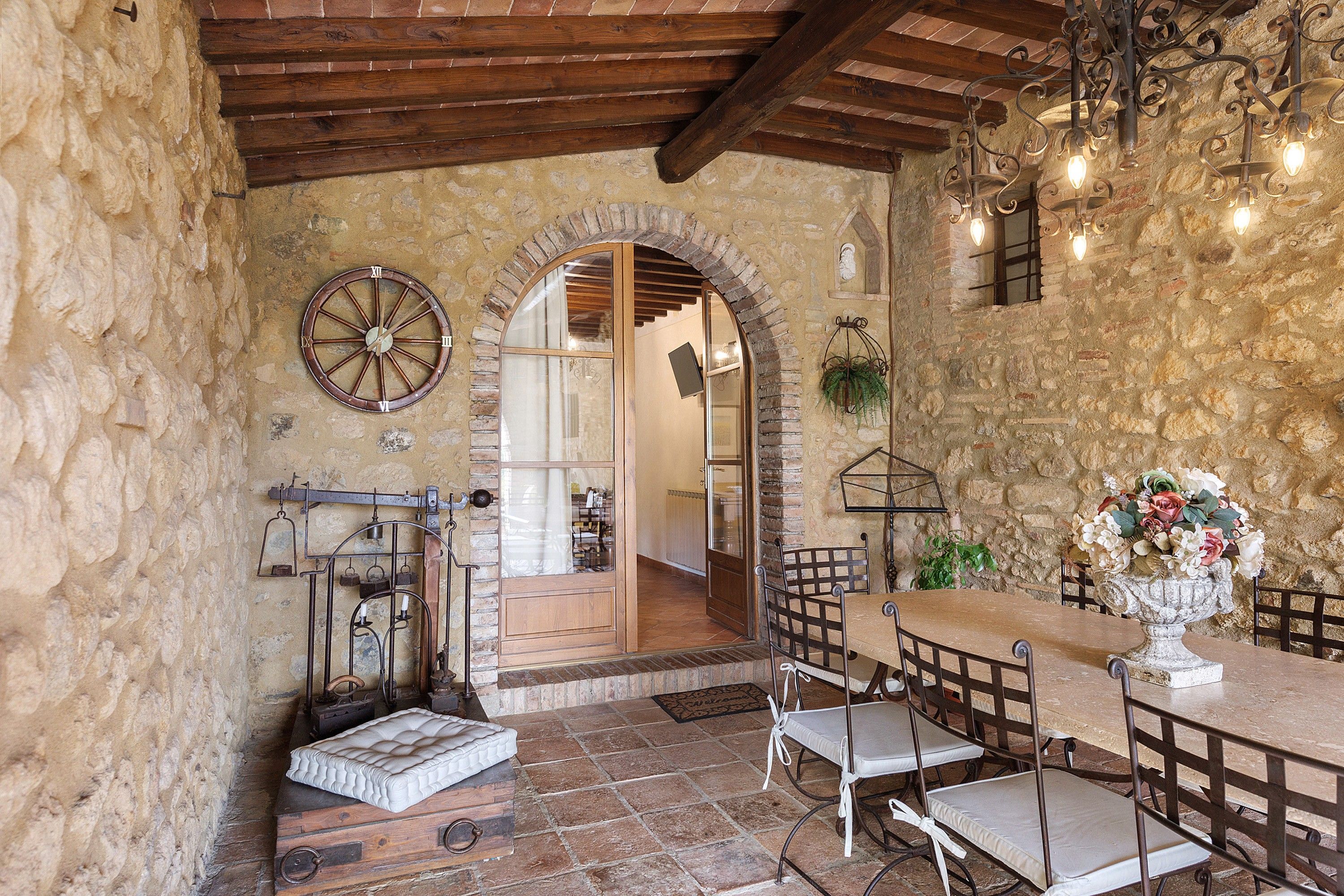 Un intérieur rustique avec des murs en pierre, un plafond en bois, une horloge ronde, une table à manger avec des chaises et un arrangement floral.