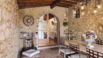 Un intérieur rustique avec des murs en pierre, un plafond en bois, une horloge ronde, une table à manger avec des chaises et un arrangement floral.