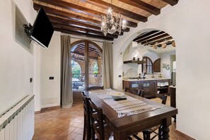 A dining area with a wooden table, chairs, a chandelier, and a TV mounted on the wall. - Apartment 'Podere Del Botruccio - Girasole' with Shared Pool, Garden & Wi-Fi (Pomarance)