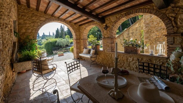 Patio esterno con archi in pietra, un tavolo con una candela e piante in vaso.