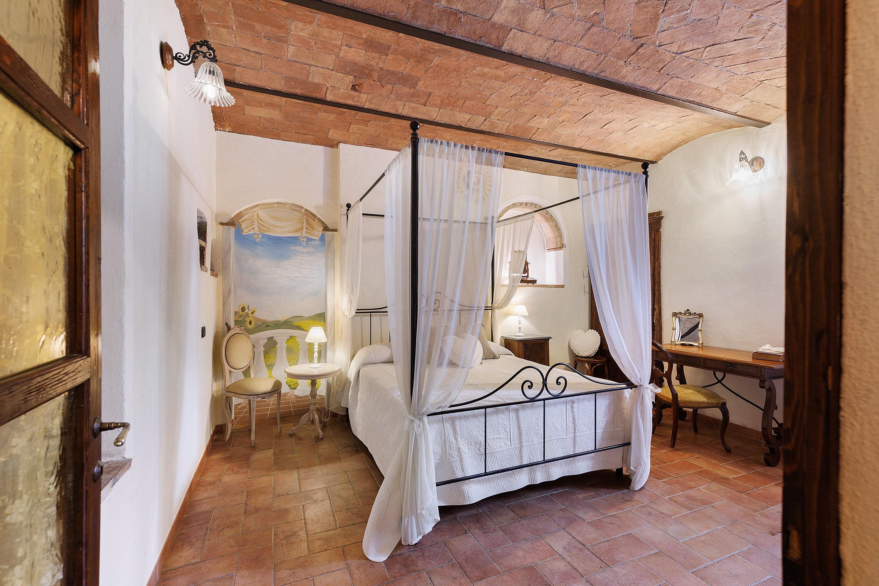 Una habitación con cama con dosel, una mesita con lámpara, una silla y un escritorio con espejo.