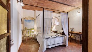 Una habitación con cama con dosel, una mesita con lámpara, una silla y un escritorio con espejo.