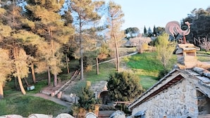Un edificio in pietra dal design rustico, una scala in pietra che conduce a una zona coperta, e vista su un paesaggio verde e lussureggiante con alberi.