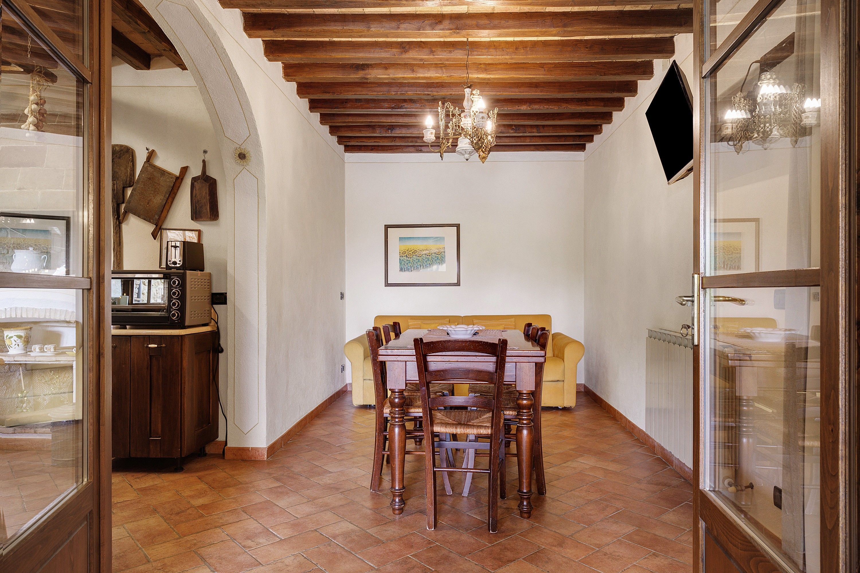 A dining area with a wooden table and chairs, a chandelier, and a painting on the wall.