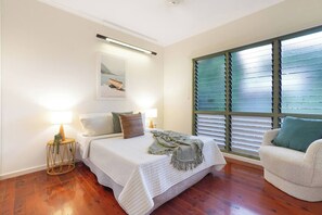 Une chambre à coucher avec un lit, des lampes de chevet, une fenêtre avec des stores et une chaise.