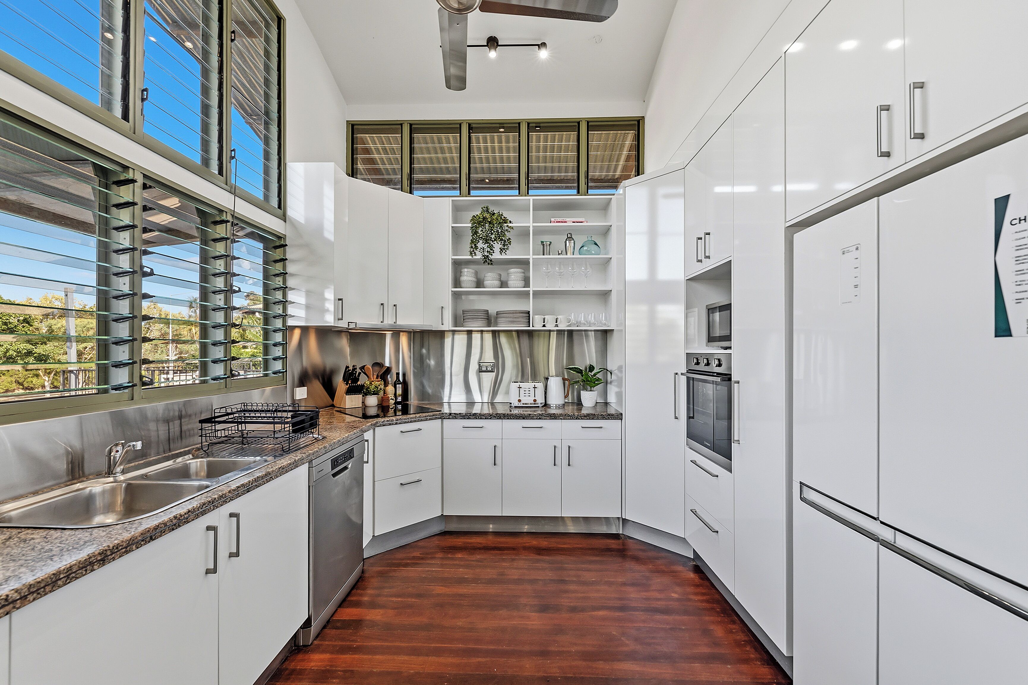 Une cuisine moderne avec des meubles blancs, des appareils électroménagers en acier inoxydable et un plancher en bois.