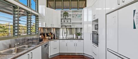 Une cuisine moderne avec des meubles blancs, des appareils électroménagers en acier inoxydable et un plancher en bois.