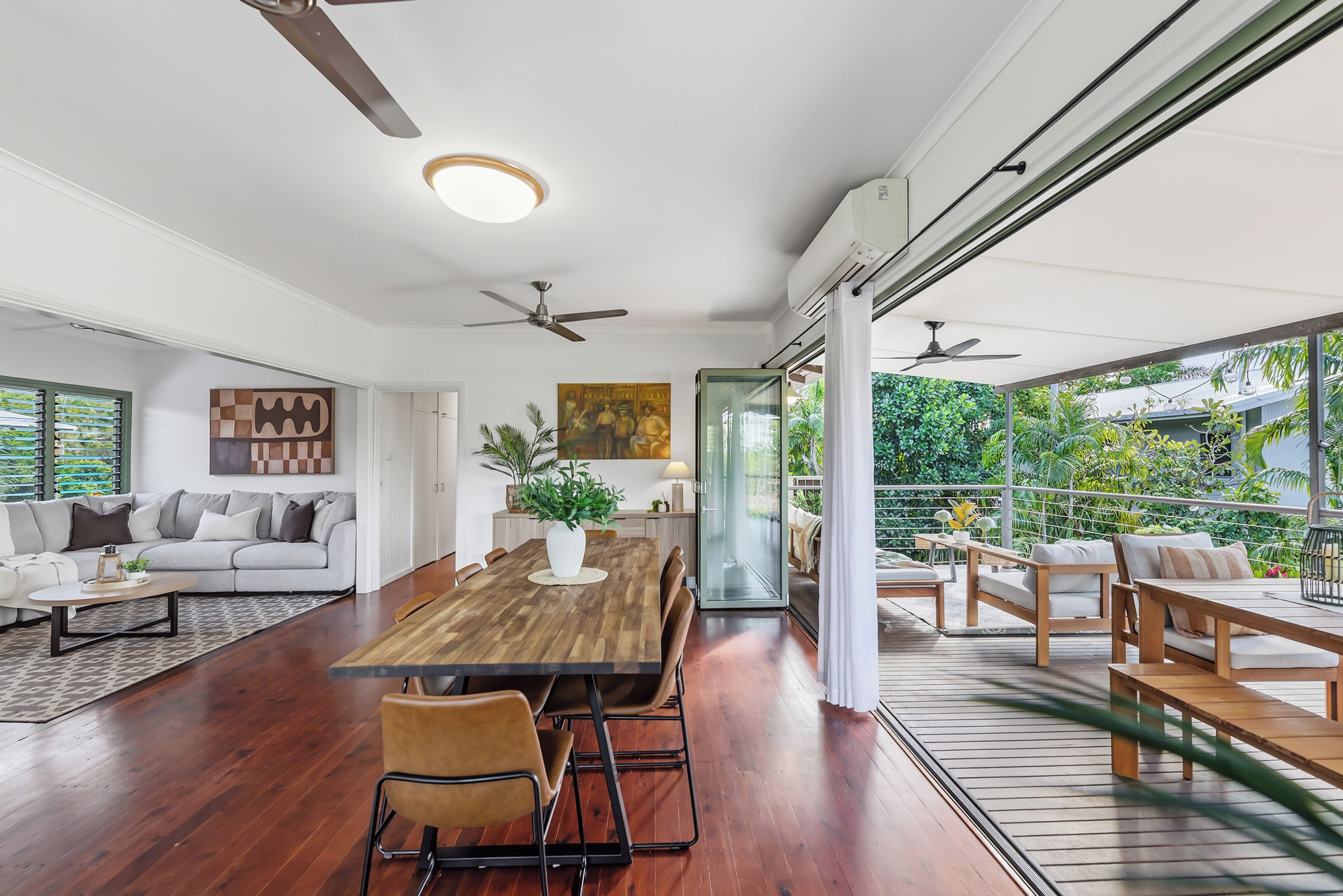 A spacious living area with a wooden dining table, comfortable seating, and a large window offering a view of greenery.
